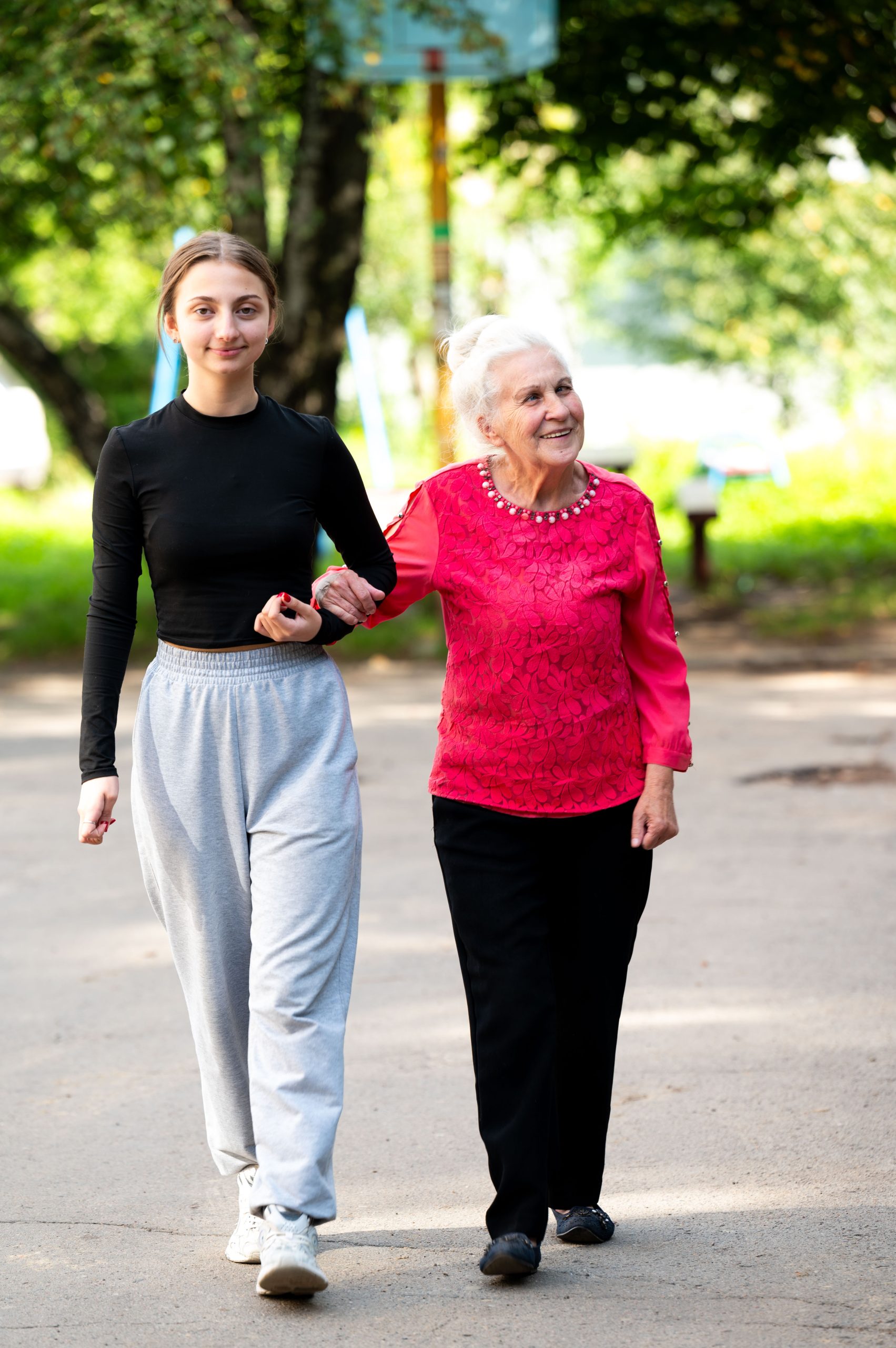 Young woman and elderly lady enjoy a sunny day walking together through a green neighborhood filled with laughter and companionship while showcasing the beauty of their bond
